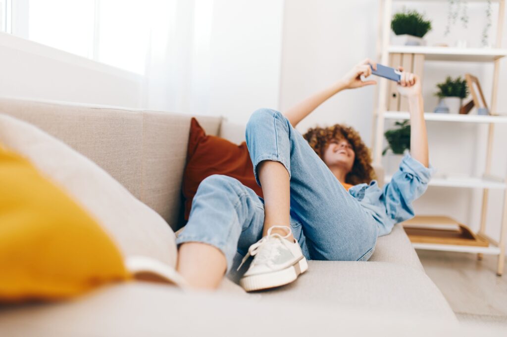 Relaxed Smiling Woman Holding Smartphone on Cozy Sofa in Living Room